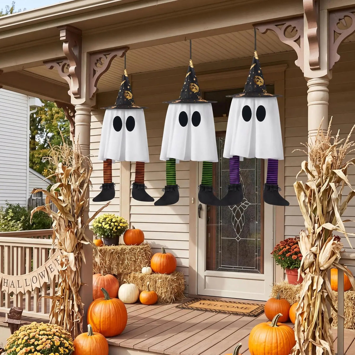 Three outdoor hanging ghosts with orange, green, and purple striped legs on a porch in daylight