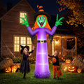 Giant 12 ft inflatable witch glowing purple in a Halloween front yard with jack-o'-lanterns and kids