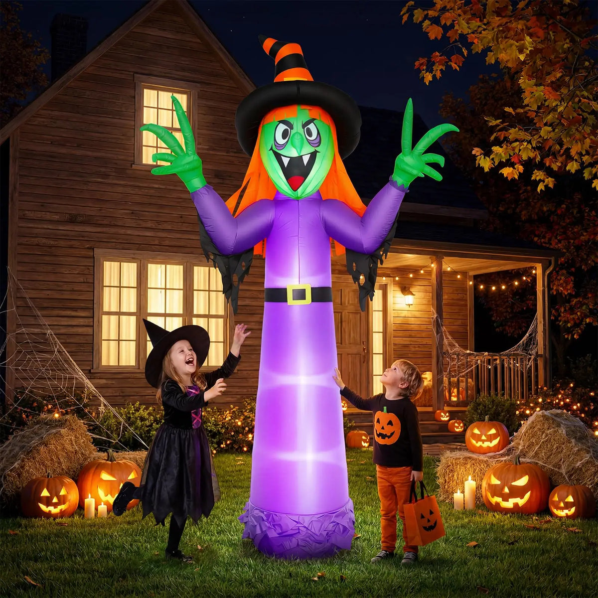 Giant 12 ft inflatable witch glowing purple in a Halloween front yard with jack-o'-lanterns and kids